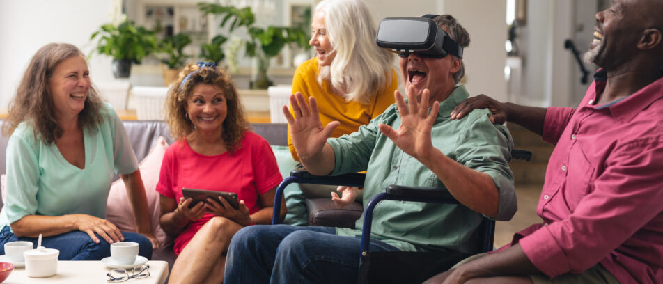 Heureux homme et femme âgés multiraciaux avec un ami handicapé utilisant un casque VR à la maison